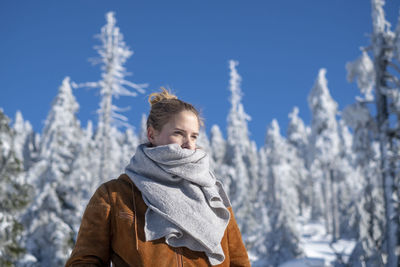 Young woman wearing warm clothing while looking away against trees during winter