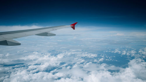 Cropped image of aircraft wing flying over clouds against sky