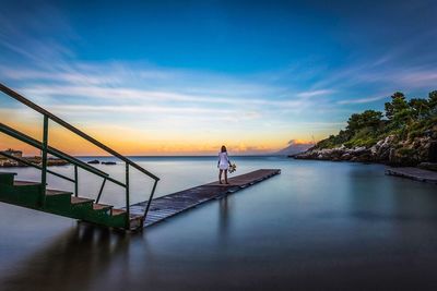 Full length of woman standing on pier by sea against sky during sunset