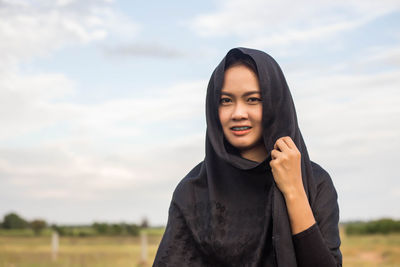 Portrait of smiling young woman standing on field against sky