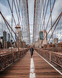 Rear view of man walking on footbridge against sky