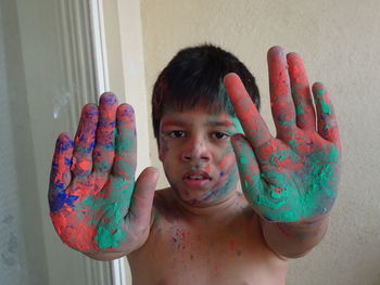 Portrait of shirtless boy showing colorful hands indoors
