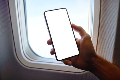 Cropped hand of man holding blank mobile phone in airplane