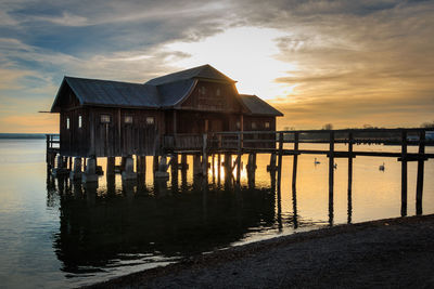 Wooden posts in sea against sky during sunset