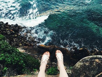 Low section of woman dangling legs over sea