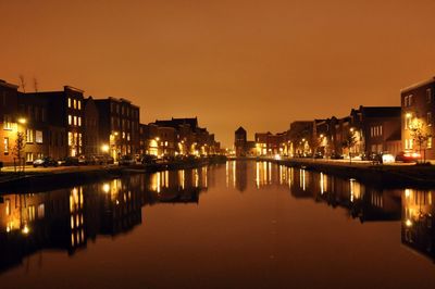 Illuminated houses by river against sky at night
