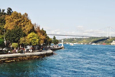 People on riverbank against clear sky