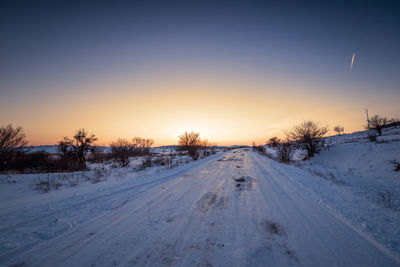 Winter sunset landscape with trees and field road.