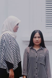 Female friends standing against white wall