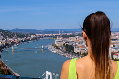 Rear view of woman looking at cityscape against sky