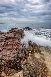 Waves splashing on rocky shore against sky