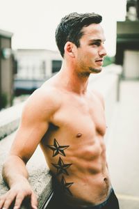 Shirtless young man standing by retaining wall on building terrace