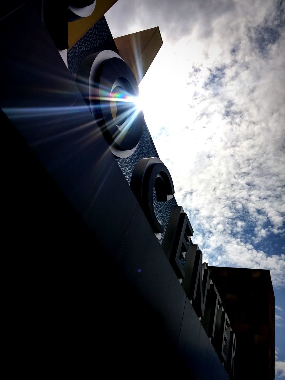 low angle view, built structure, architecture, building exterior, sky, cloud - sky, sunlight, building, outdoors, no people, cloud, day, city, cloudy, sunbeam, tilt, lens flare, sun, part of, tower