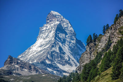 Low angle view of snowcapped mountains against clear blue sky