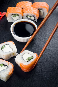 Fresh tasty sushi with salmon in wooden chopsticks on a dark background. 