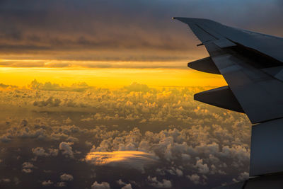 Cropped image of airplane flying over clouds during sunset