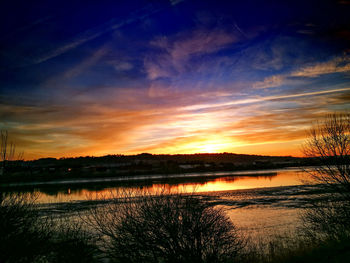 Scenic view of lake against dramatic sky during sunset