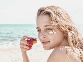 Portrait of woman holding sunglasses at beach against sky