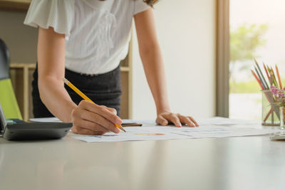 Midsection of woman holding paper while standing on table