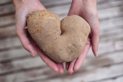 Cropped hands of woman holding heart shape raw potato over table