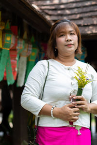 Portrait of woman with bouquet standing against temple