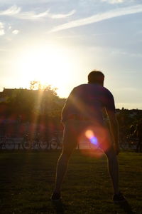 Rear view of man on field against sky during sunset