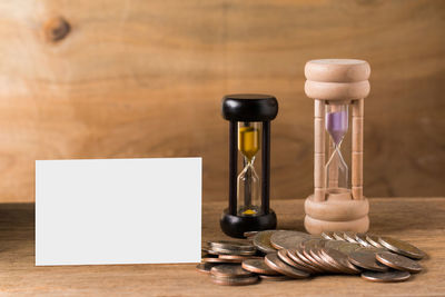 Close-up of blank paper with hourglasses and coins on wooden table