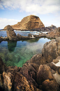 Rock formations on sea against cloudy sky