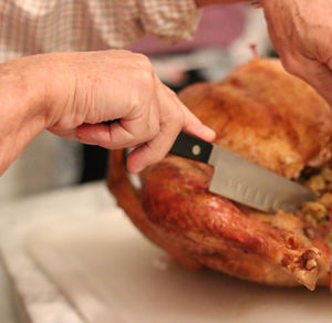 Cropped hand cutting chicken meat on table