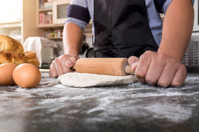 Midsection of man rolling dough on table 