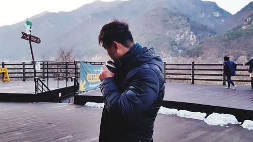 Man drinking while standing against mountain during winter