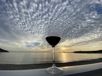 Wine glass on sea against sky during sunset