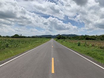 Empty road amidst field against sky