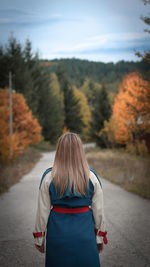 Rear view of woman standing on road against sky during autumn