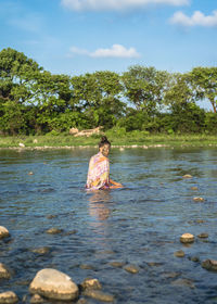 Woman bathing in river with mud facial mask against sky