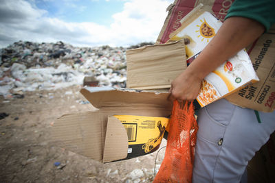 Midsection of man holding garbage against sky
