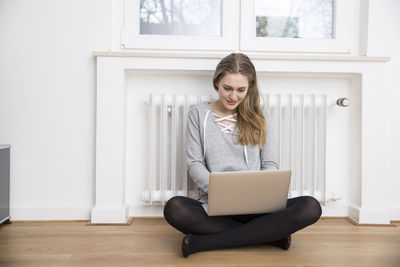 Young woman sitting on the floor in front of heater using laptop