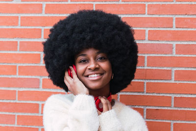 Carefree afro woman with white perfect smile and white jumper listening to music with red headphones