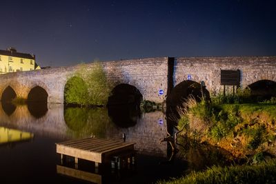 Arch bridge over river against buildings at night
