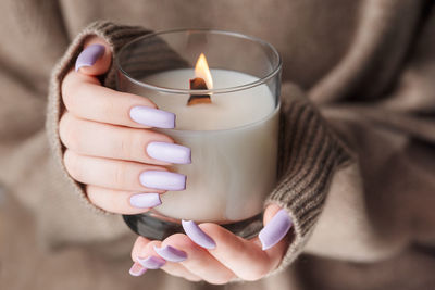 The hands of a young girl with a beautiful light purple manicure hold a candle. 