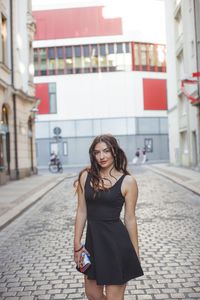 Portrait of young woman standing against building in city