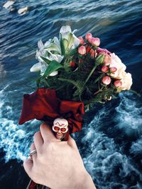 Close-up of hand holding flower bouquet over sea