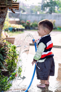 Adorable asian toddler boy plays and enjoys having fun watering garden flowers and lawn 