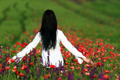 Rear view of woman with red flower on field