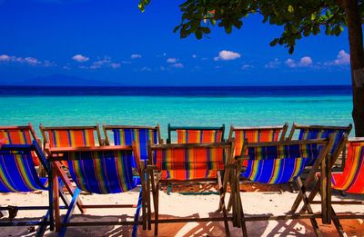 Chairs and tables on beach against blue sky