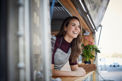 Smiling young woman looking away while standing in food truck at city