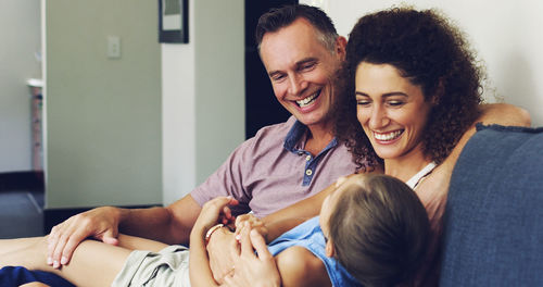 Happy parents with daughter sitting on sofa at home