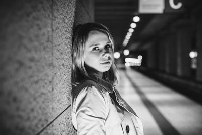 Portrait of young woman leaning on wall at night