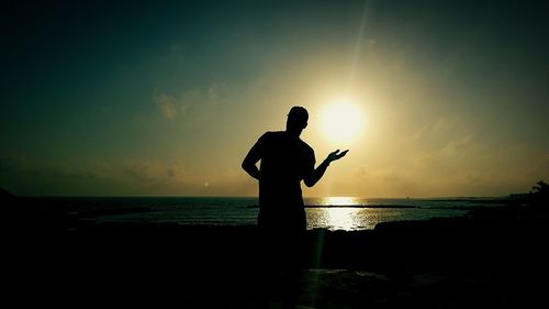 Silhouette man standing on beach against sky during sunset