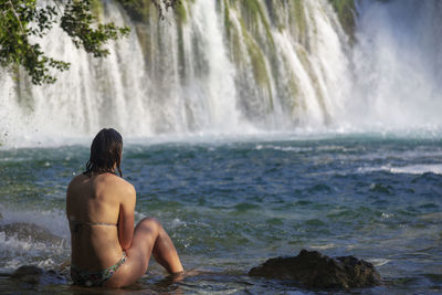 Rear view of shirtless man looking at waterfall
